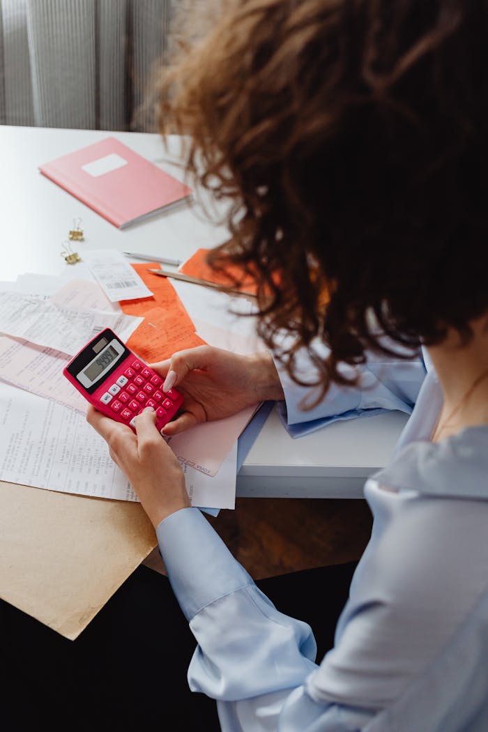 Adult woman working with receipts and a bright pink calculator at a desk, focusing on finances.
